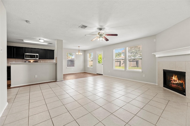 unfurnished living room featuring visible vents, ceiling fan, a textured ceiling, a fireplace, and light tile patterned flooring