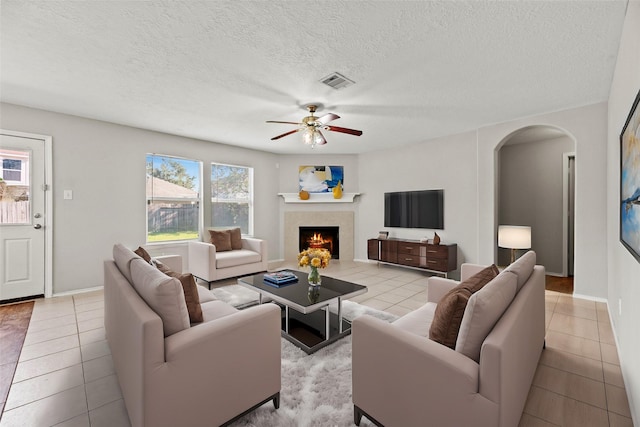 living room with a warm lit fireplace, visible vents, light tile patterned floors, and arched walkways