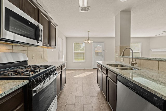 kitchen featuring decorative backsplash, light stone countertops, wood tiled floor, stainless steel appliances, and a sink