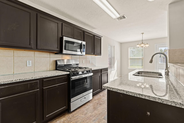 kitchen featuring visible vents, light stone counters, a sink, stainless steel appliances, and backsplash