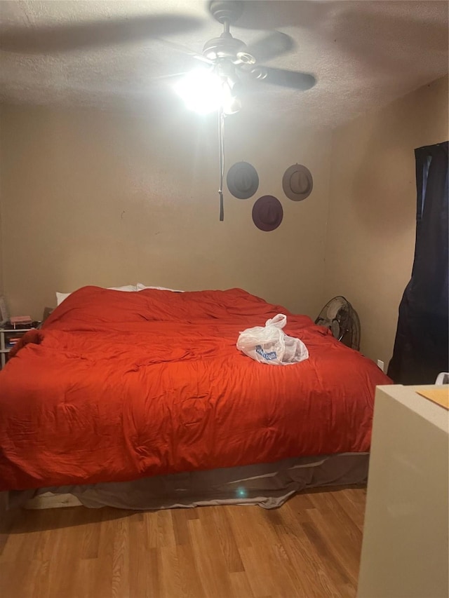 bedroom with ceiling fan, wood-type flooring, and a textured ceiling