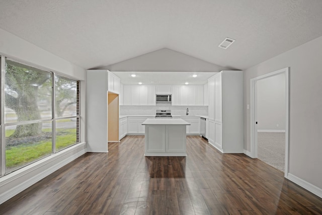 kitchen with appliances with stainless steel finishes, dark hardwood / wood-style flooring, a kitchen island, white cabinets, and backsplash