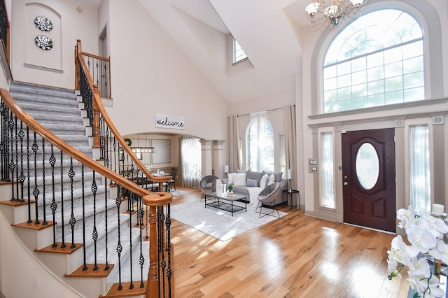 foyer featuring an inviting chandelier, high vaulted ceiling, decorative columns, and light wood-type flooring