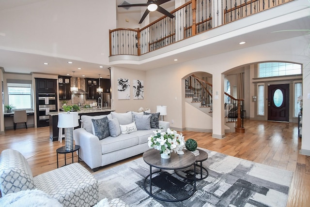 living room with ceiling fan, a towering ceiling, and light hardwood / wood-style flooring