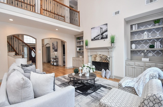 living room with built in shelves, a towering ceiling, a tiled fireplace, and light hardwood / wood-style floors