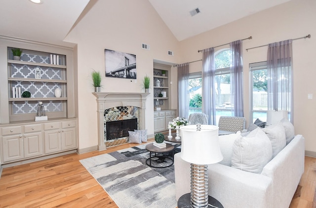 living room featuring high vaulted ceiling, built in features, a fireplace, and light hardwood / wood-style flooring