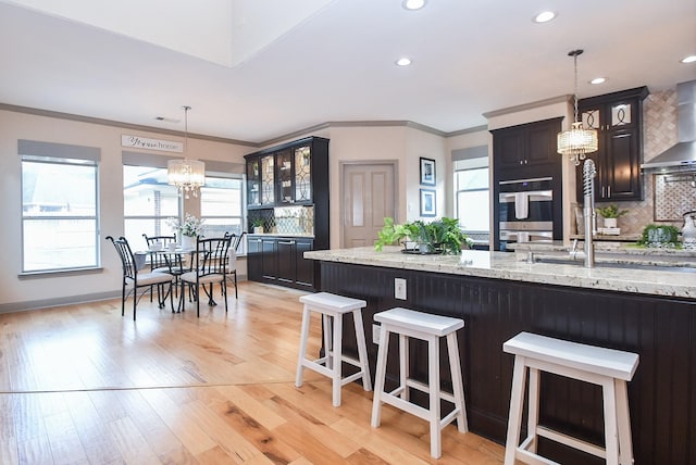 kitchen with a breakfast bar area, light stone counters, hanging light fixtures, double oven, and backsplash