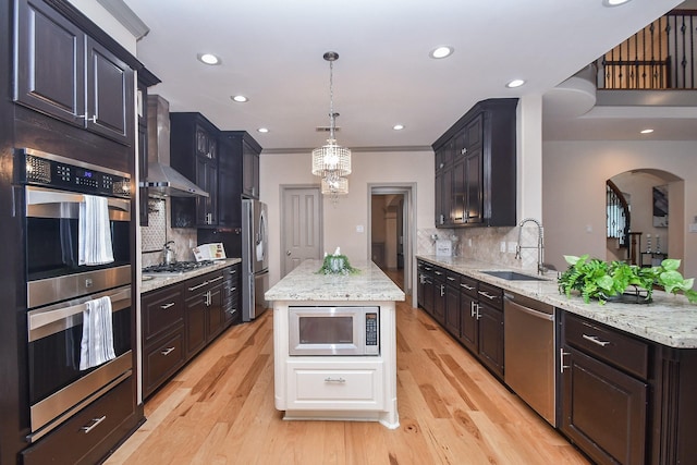 kitchen featuring wall chimney exhaust hood, sink, decorative light fixtures, a kitchen island, and stainless steel appliances