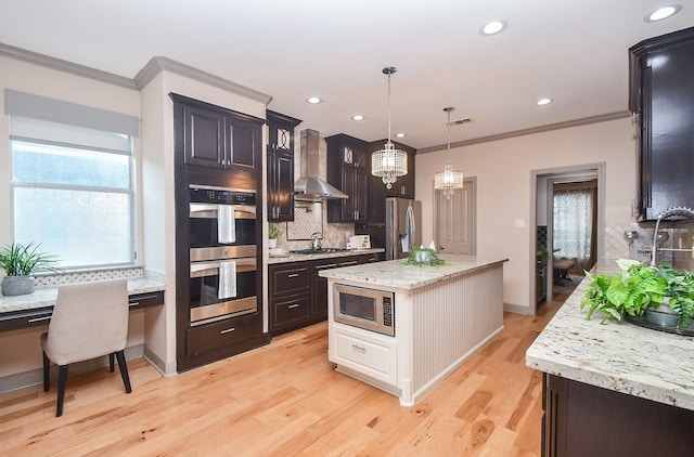 kitchen featuring crown molding, decorative light fixtures, appliances with stainless steel finishes, a kitchen island, and wall chimney range hood