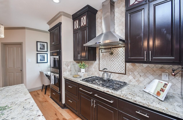 kitchen featuring wall chimney exhaust hood, light wood-type flooring, ornamental molding, stainless steel gas stovetop, and decorative backsplash