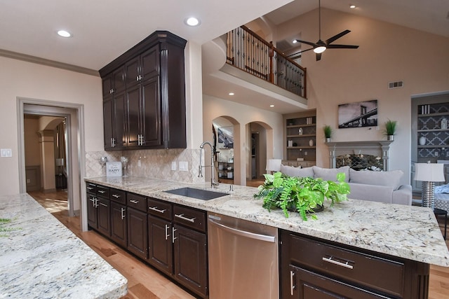 kitchen with stainless steel dishwasher, light stone countertops, sink, and dark brown cabinets