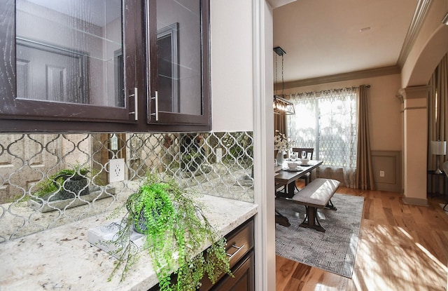 interior space with backsplash, hardwood / wood-style flooring, light stone counters, dark brown cabinetry, and crown molding