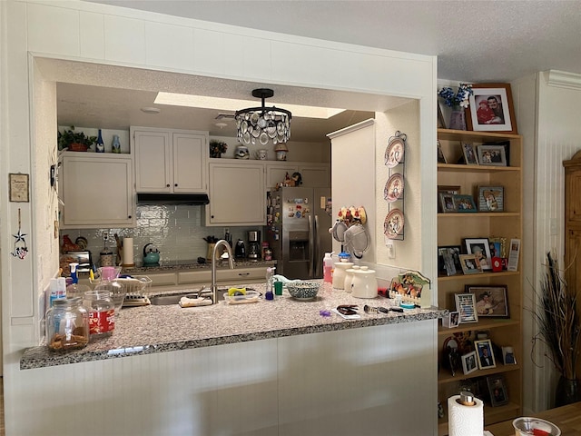 kitchen with stainless steel refrigerator with ice dispenser, decorative backsplash, decorative light fixtures, and light stone counters