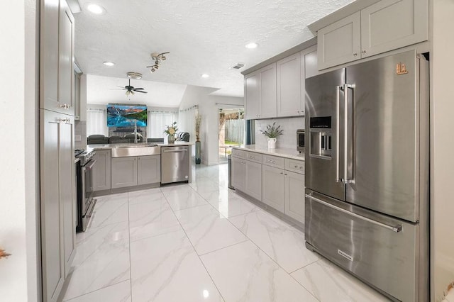 kitchen featuring sink, a textured ceiling, appliances with stainless steel finishes, gray cabinets, and kitchen peninsula