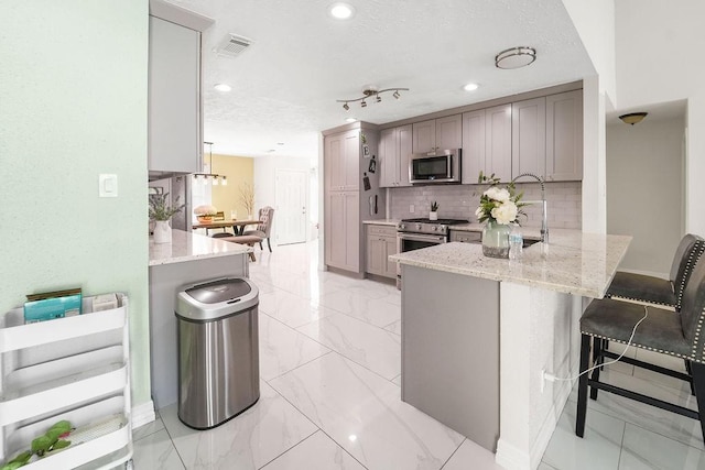 kitchen featuring a breakfast bar area, appliances with stainless steel finishes, gray cabinetry, backsplash, and kitchen peninsula