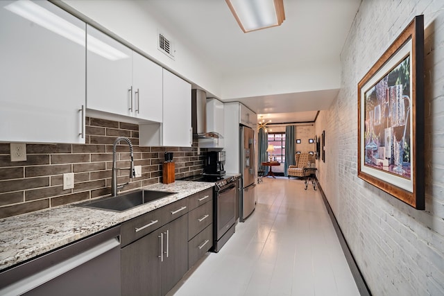 kitchen with sink, white cabinetry, dark brown cabinets, appliances with stainless steel finishes, and wall chimney range hood