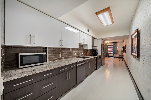 kitchen with brick wall, sink, white cabinets, stainless steel appliances, and dark brown cabinets