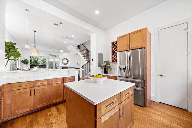 kitchen featuring stainless steel fridge, a kitchen island, a peninsula, light countertops, and pendant lighting