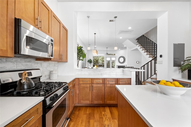 kitchen with brown cabinetry, appliances with stainless steel finishes, a peninsula, light countertops, and light wood-style floors