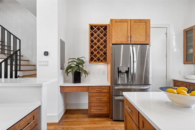 kitchen with stainless steel fridge, glass insert cabinets, brown cabinetry, and light countertops