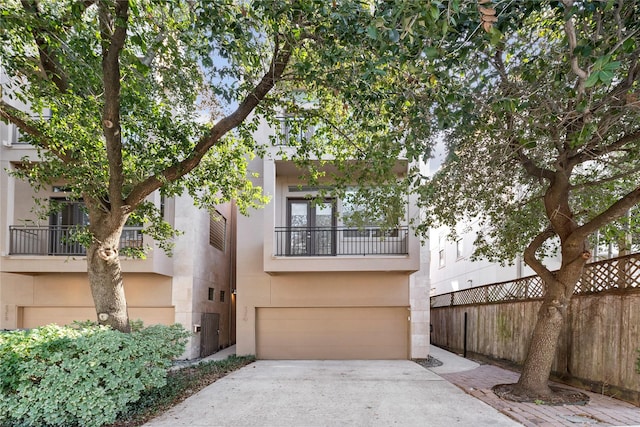 view of front facade with concrete driveway, a balcony, an attached garage, fence, and stucco siding