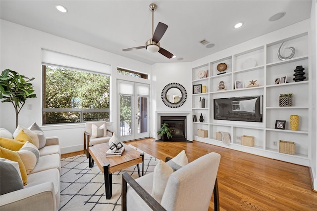 living room featuring a fireplace with flush hearth, french doors, visible vents, and light wood finished floors