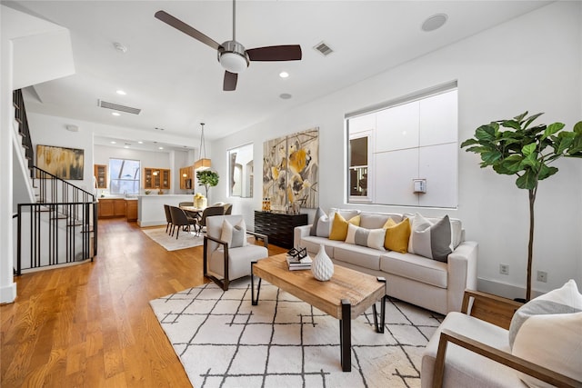 living room featuring stairs, light wood-type flooring, visible vents, and a ceiling fan