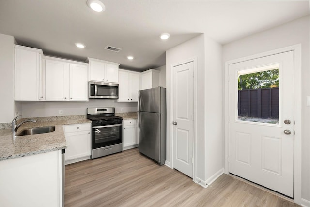 kitchen featuring sink, white cabinetry, light stone counters, light wood-type flooring, and stainless steel appliances