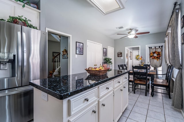 kitchen featuring light tile patterned floors, stainless steel fridge, a center island, white cabinets, and dark stone counters