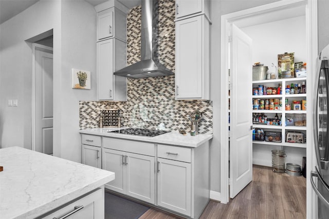 kitchen featuring backsplash, dark hardwood / wood-style flooring, black electric stovetop, light stone countertops, and wall chimney range hood