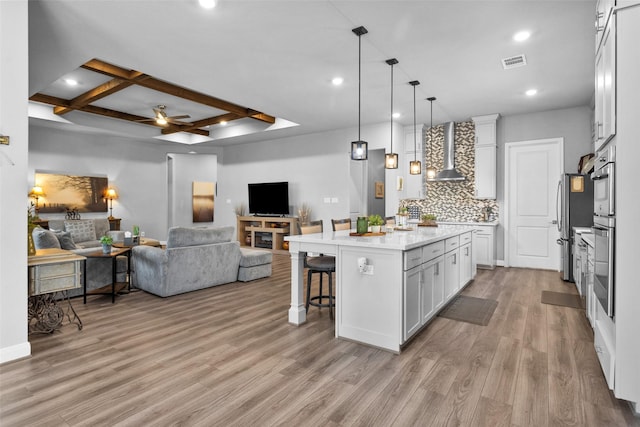 kitchen with pendant lighting, white cabinetry, an island with sink, a kitchen bar, and wall chimney exhaust hood