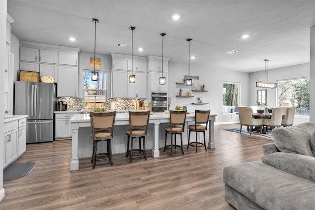 kitchen with a breakfast bar area, backsplash, stainless steel appliances, a kitchen island, and decorative light fixtures