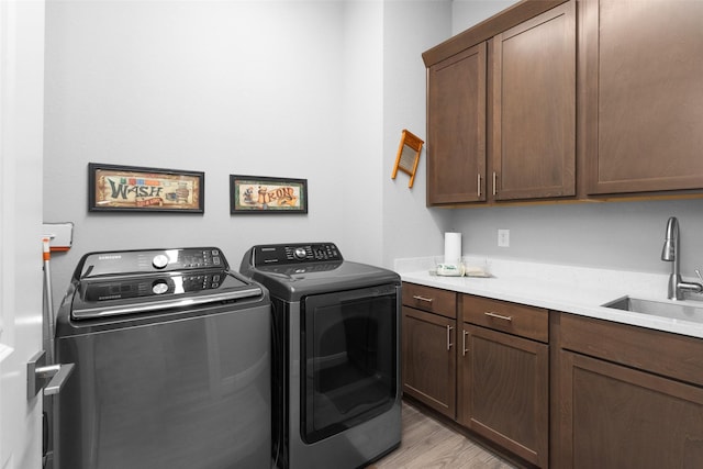 laundry area with light hardwood / wood-style floors, cabinets, washer and clothes dryer, and sink