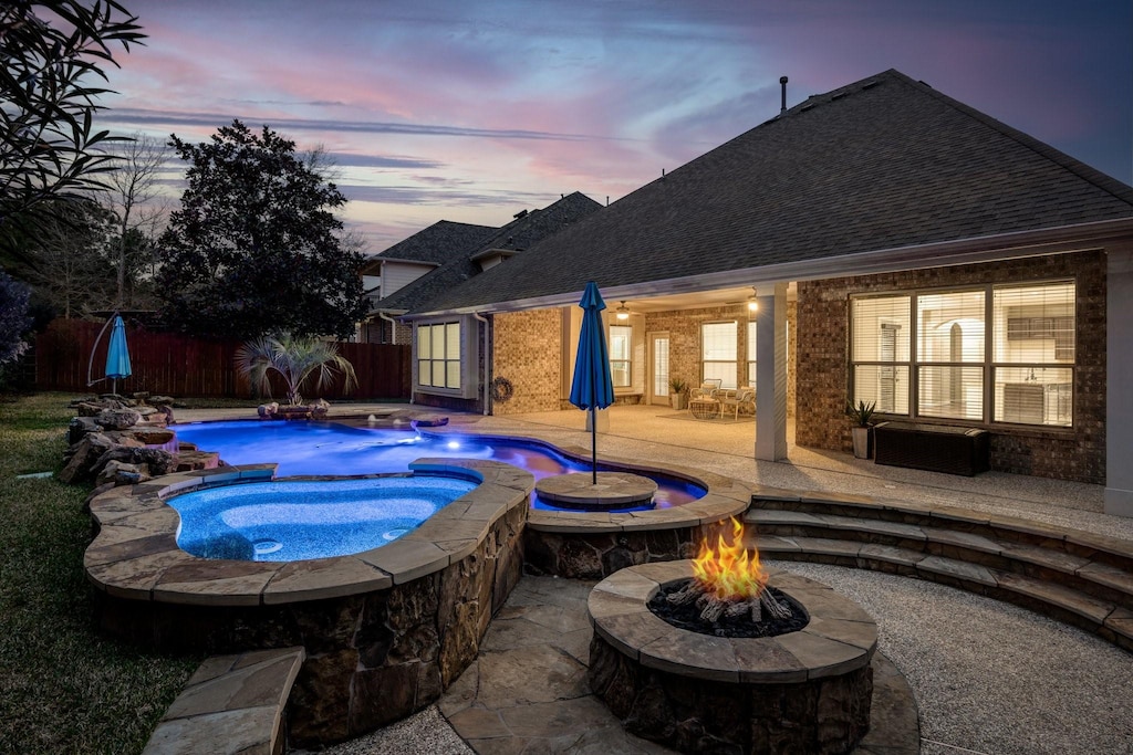 pool at dusk featuring an in ground hot tub, a patio, and a fire pit