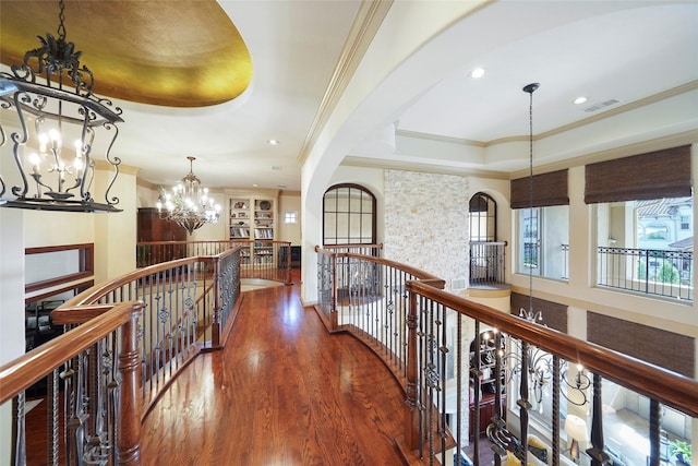 hall with visible vents, wood finished floors, an inviting chandelier, a tray ceiling, and an upstairs landing