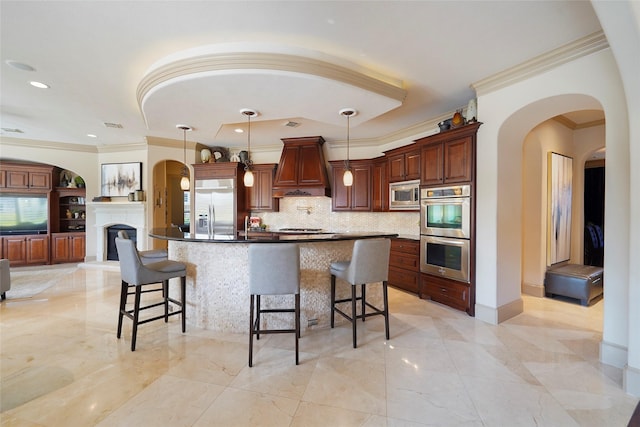 kitchen with dark countertops, custom range hood, a breakfast bar, built in appliances, and hanging light fixtures