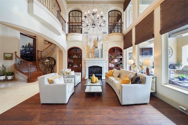 living area with a chandelier, dark wood-style flooring, built in features, stairway, and a glass covered fireplace