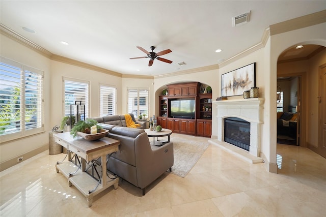 living area featuring arched walkways, recessed lighting, visible vents, a glass covered fireplace, and crown molding