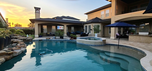 pool at dusk with a patio, a bar, fence, and a pool with connected hot tub