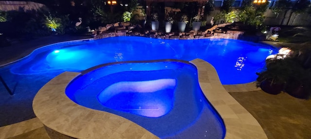 pool at night featuring a pool with connected hot tub