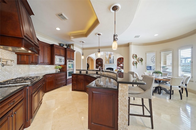 kitchen with arched walkways, pendant lighting, a center island with sink, stainless steel appliances, and a sink