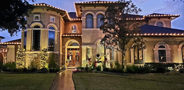 mediterranean / spanish house featuring a front lawn, a tile roof, and stucco siding