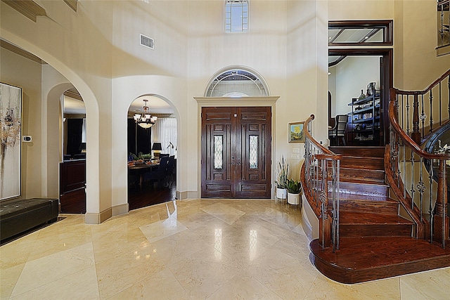 foyer featuring arched walkways, a high ceiling, visible vents, baseboards, and stairway