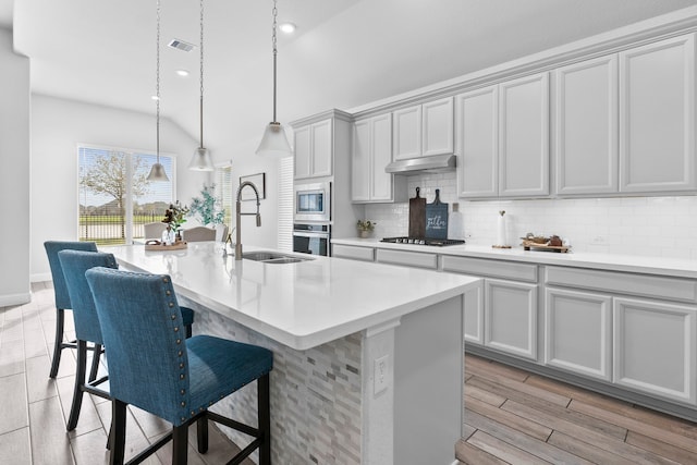 kitchen with pendant lighting, an island with sink, sink, backsplash, and stainless steel appliances