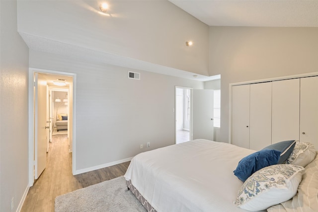 bedroom with high vaulted ceiling, light hardwood / wood-style floors, and a closet