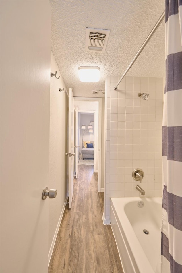 bathroom with hardwood / wood-style flooring, shower / bath combination with curtain, and a textured ceiling