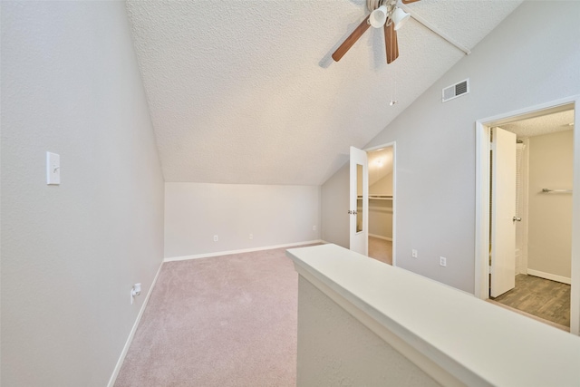 bonus room featuring lofted ceiling, ceiling fan, light carpet, and a textured ceiling