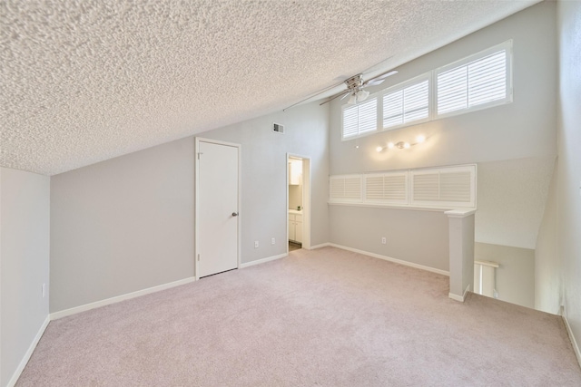 interior space featuring ceiling fan, vaulted ceiling, light carpet, and a textured ceiling