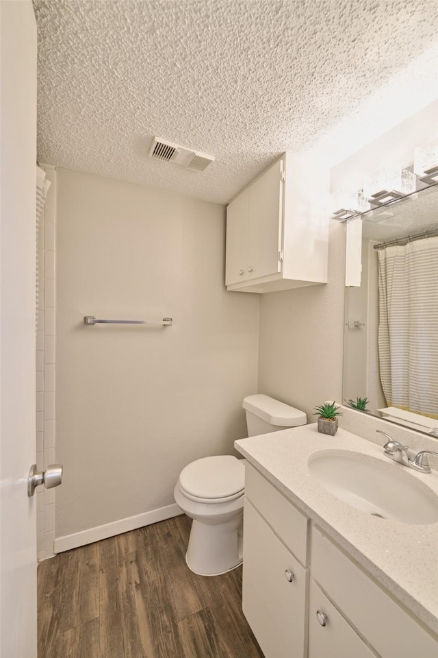 bathroom with toilet, a shower with curtain, wood-type flooring, a textured ceiling, and vanity