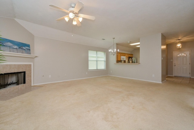 unfurnished living room featuring a tiled fireplace, ceiling fan with notable chandelier, vaulted ceiling, and light colored carpet